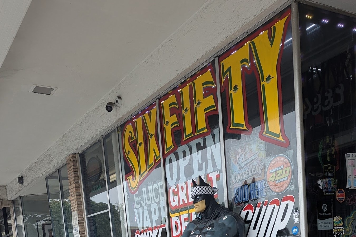Six Fifty Smoke Shop's hand-painted storefront sign on Junipero Serra Boulevard, SIX FIFTY in yellow and red lettering across the black window glass, above E-JUICE VAPE, OPEN and SHOP.