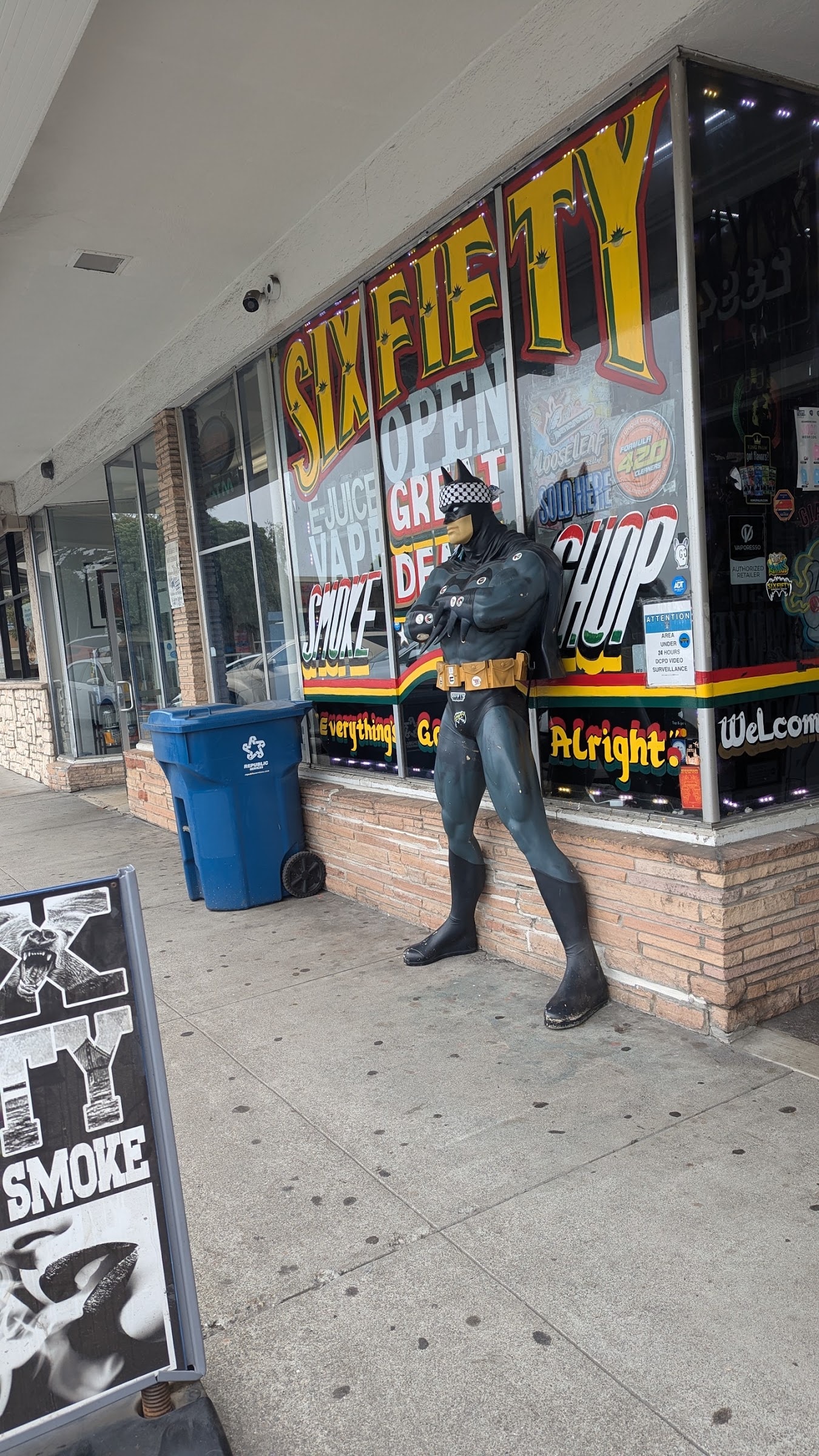 The full Six Fifty Smoke Shop storefront on Junipero Serra Boulevard, painted windows above a red, yellow and green stripe band, with the shop's black statue standing by the door.